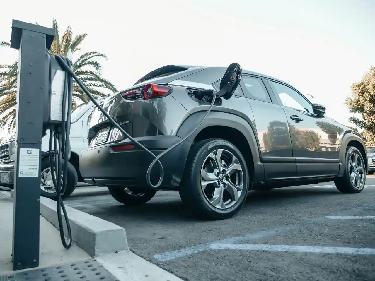 Voiture électrique branchée à une borne sur une place de parking extérieure, câble déroulé au sol.