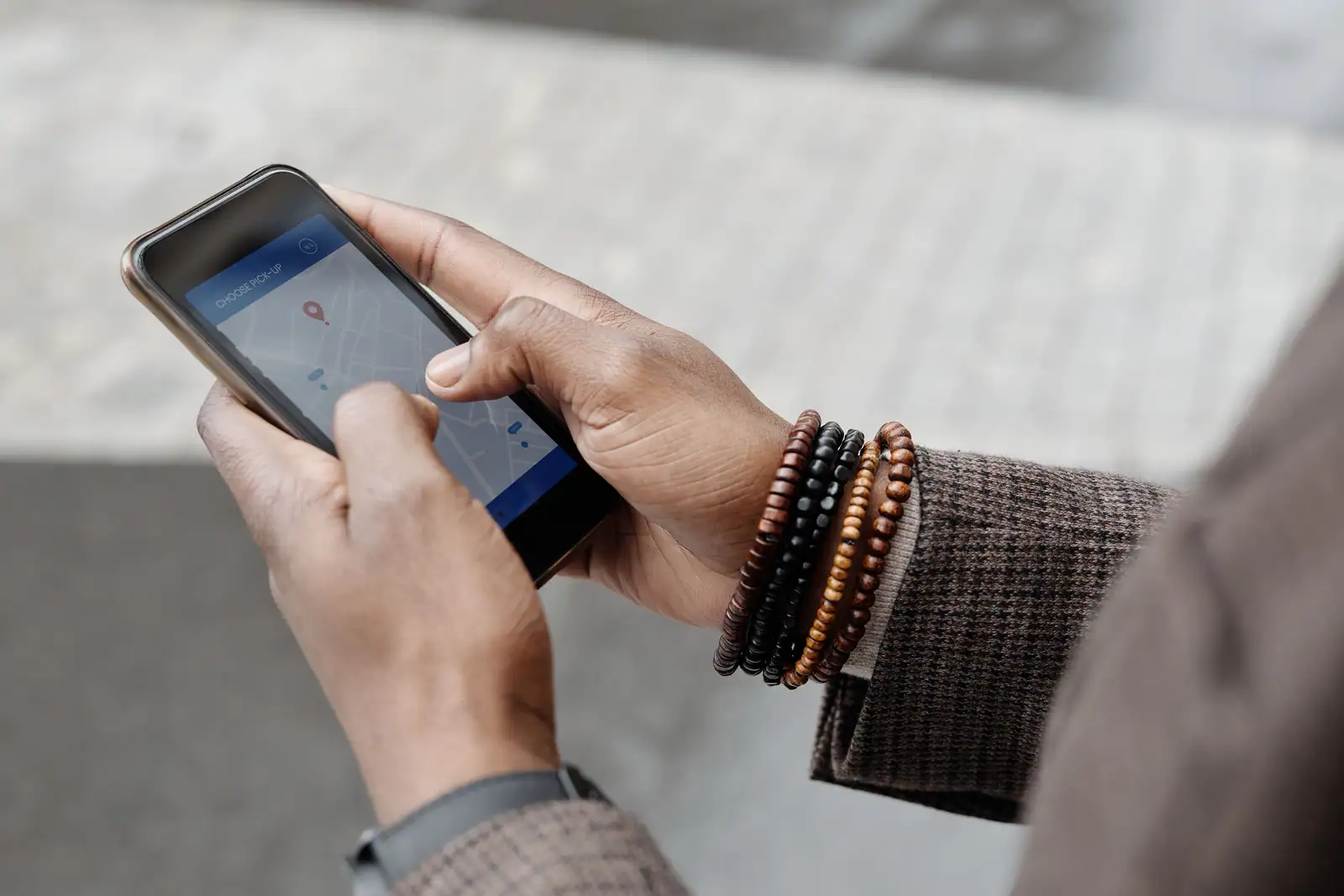 Mains tenant un smartphone qui affiche une carte avec un repère de position rouge, en extérieur
