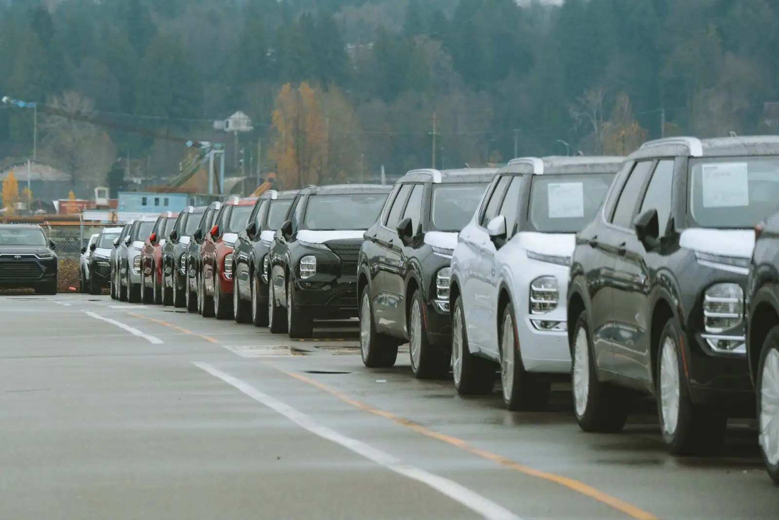 Longue file de SUV neufs de couleurs différentes alignés sur un parc extérieur, par temps gris et humide