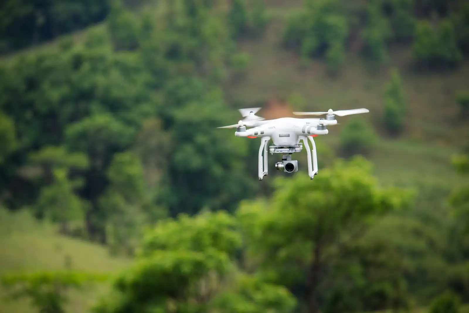 Drone quadricoptère blanc équipé d'une caméra sur nacelle, en vol au-dessus d'une végétation dense