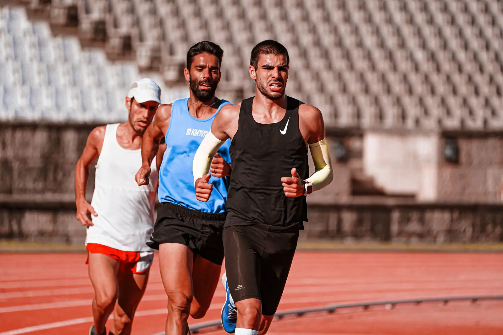 Trois coureurs de demi-fond en pleine course sur la piste rouge d'un stade d'athlétisme