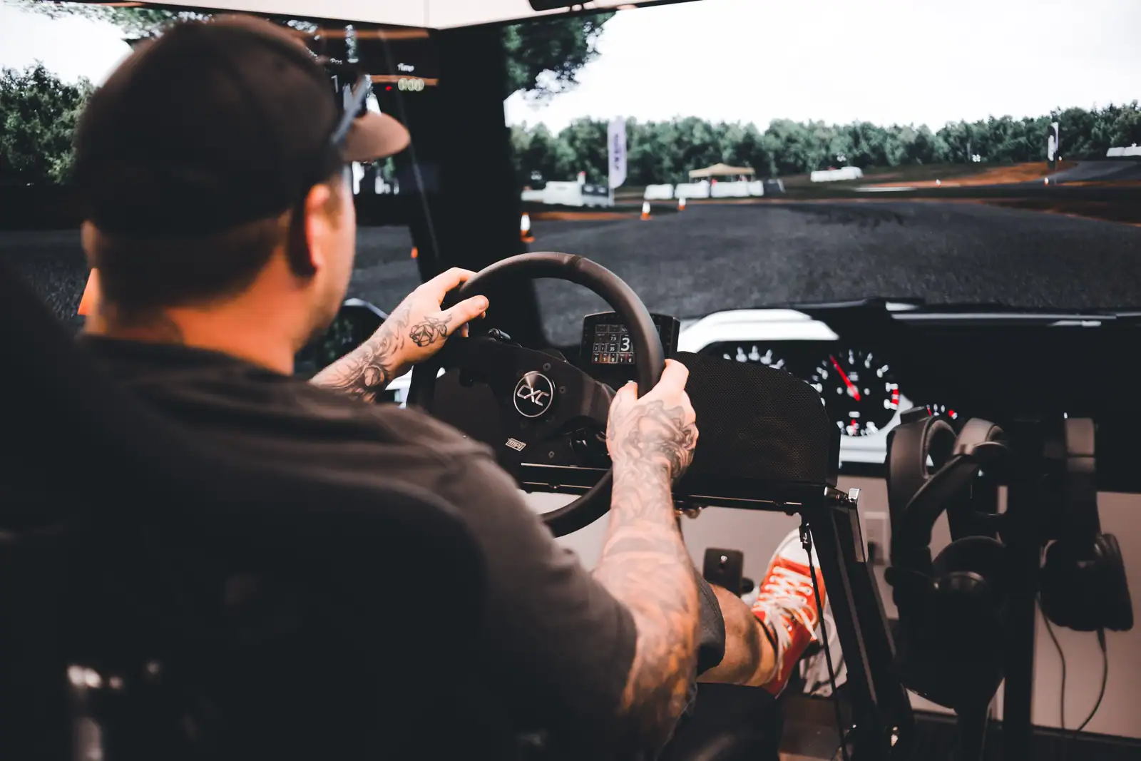 Joueur au volant d'un simulateur de course devant un grand écran affichant un circuit boisé.