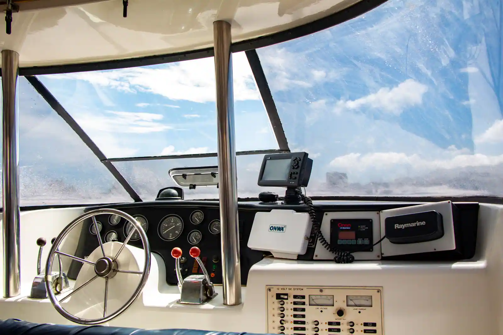 Poste de pilotage d'un bateau de plaisance avec barre à roue, compteurs et radio VHF, ciel dégagé