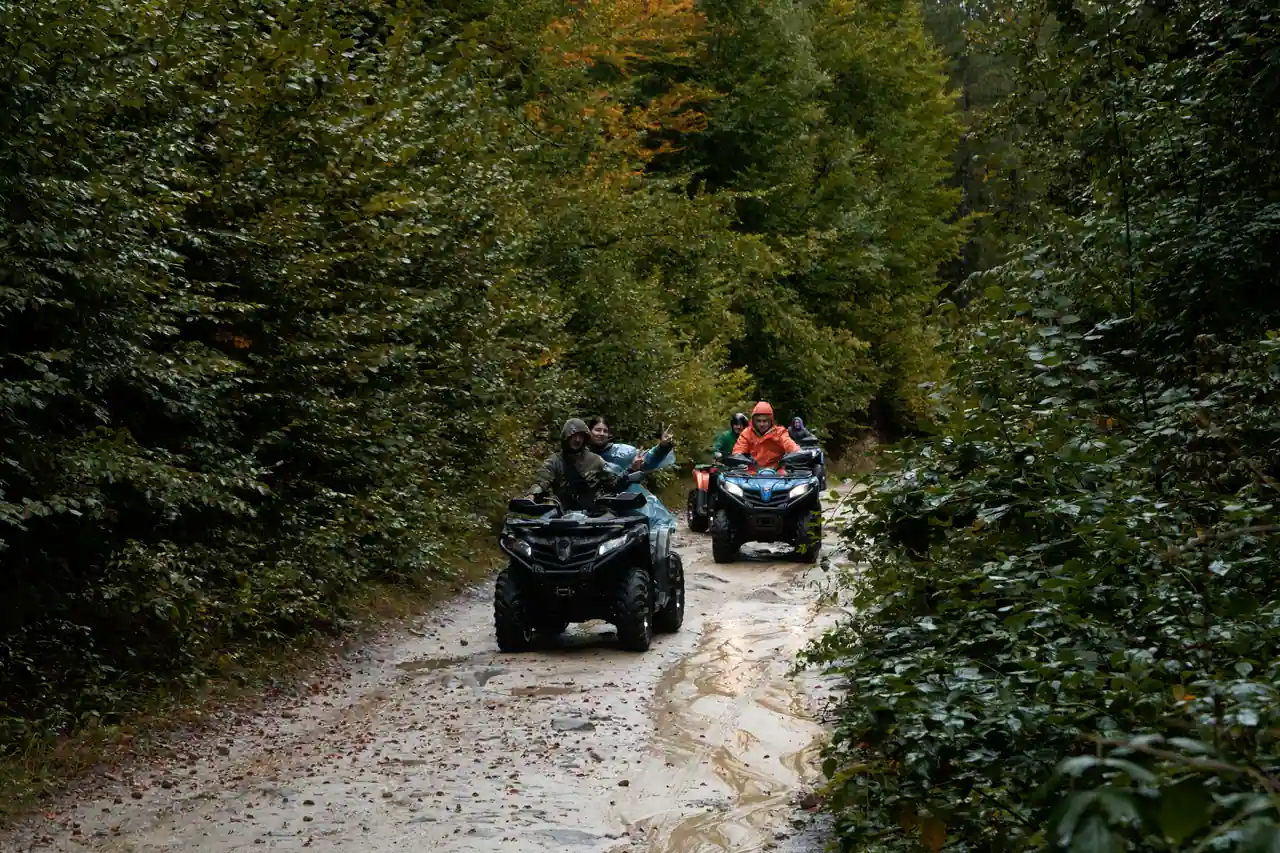 Groupe de quads tout-terrain biplaces en randonnée sur un chemin forestier boueux, sous la pluie