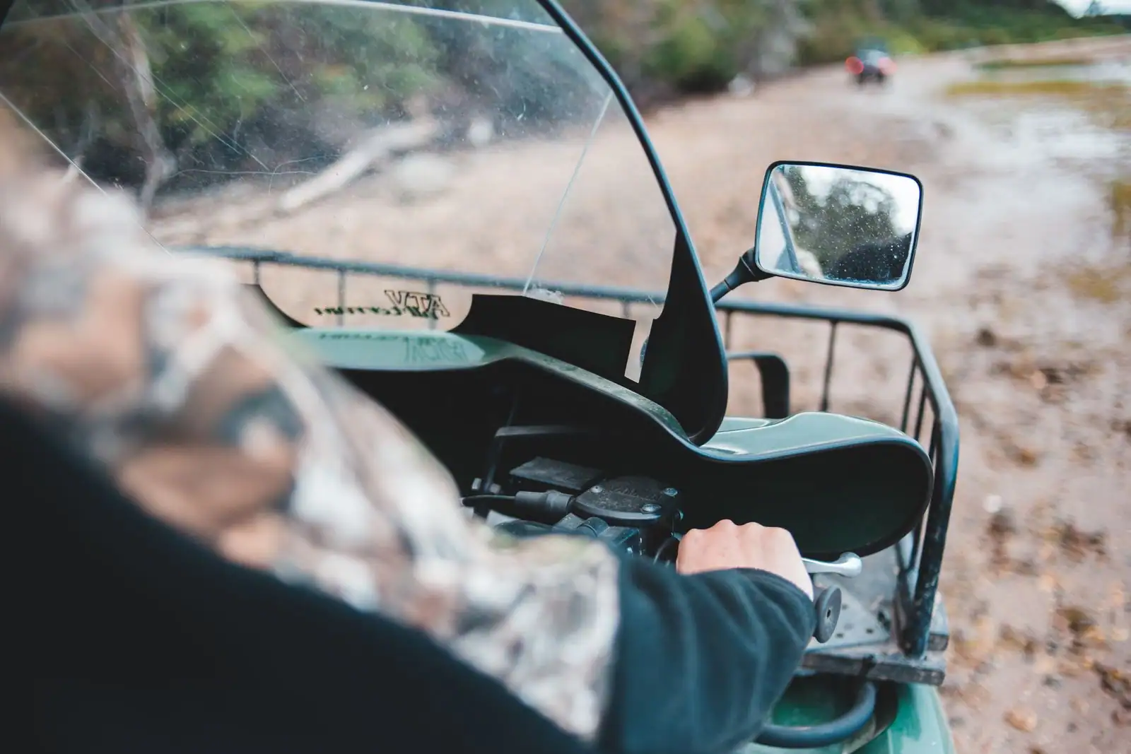 Vue depuis le guidon d'un quad utilitaire vert à pare-brise et porte-bagages, sur un chemin de terre