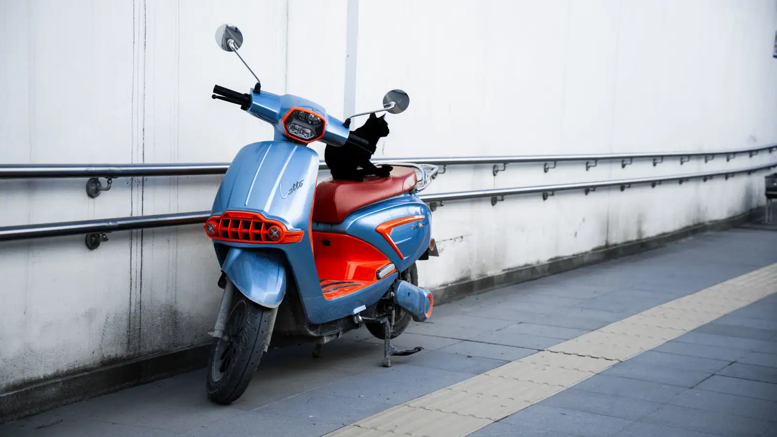 Petit scooter urbain de faible cylindrée garé le long d'un mur, béquille sortie, prêt pour un trajet court