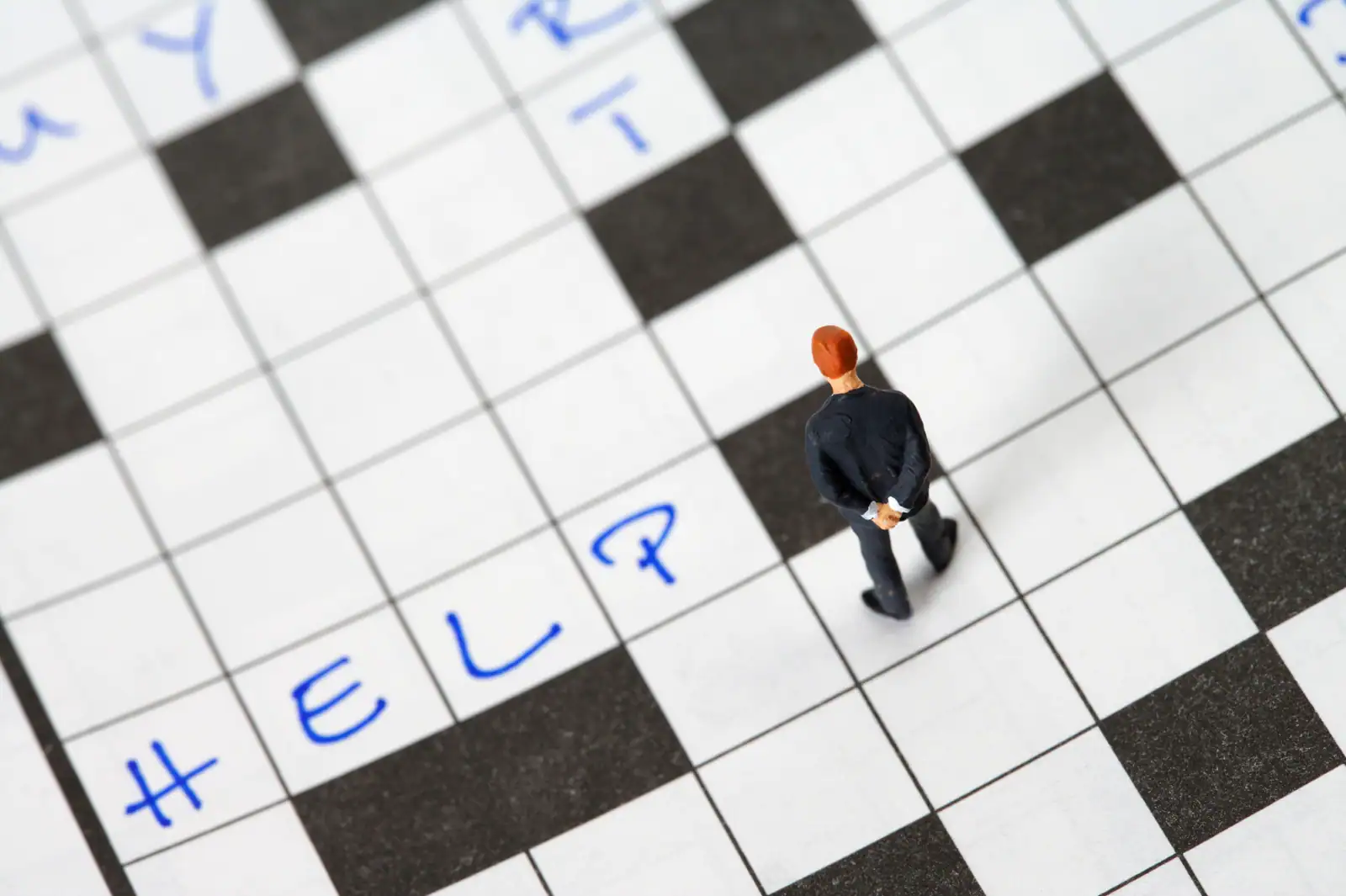Grille de mots croisés partiellement remplie au stylo bleu, avec une figurine posée sur les cases