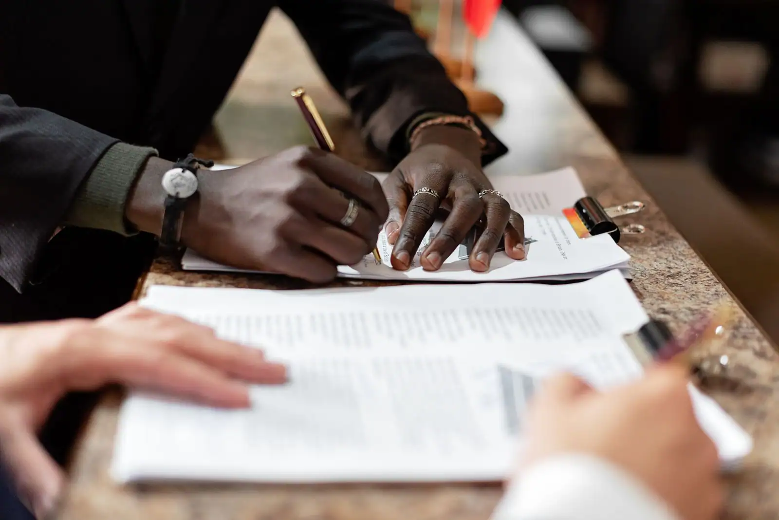 Mains remplissant et signant des documents administratifs sur un comptoir, lors d'une démarche officielle
