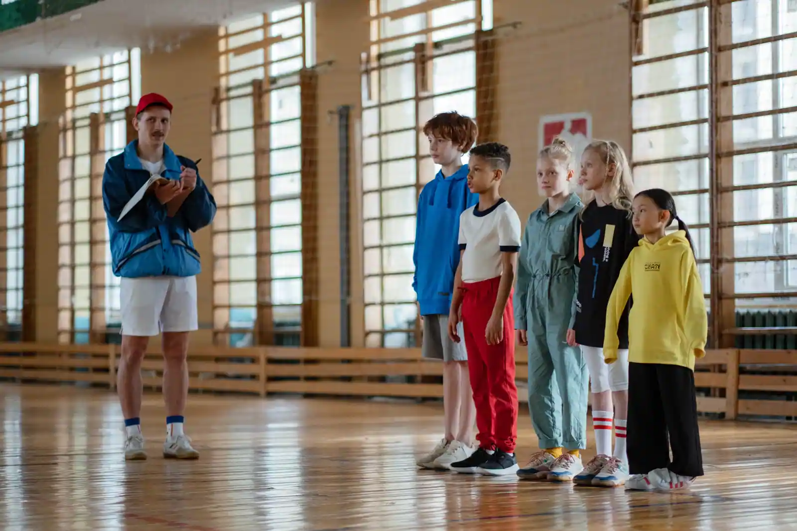 Éducateur sportif face à un groupe d'enfants alignés dans un gymnase avant le début de la séance