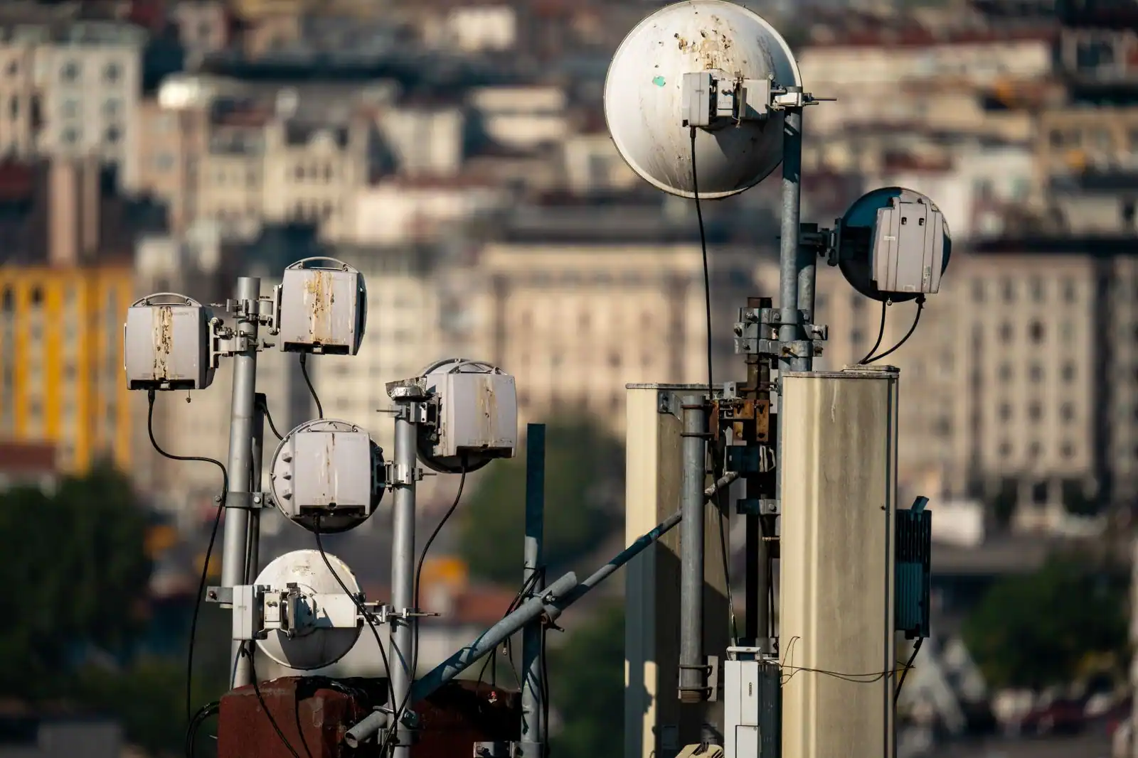 Grappe d'antennes hertziennes et de paraboles sur un toit, quartier dense flouté à l'arrière-plan