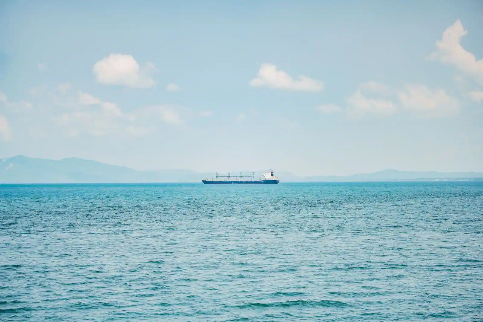 Cargo à grues de bord seul sur une mer calme, la côte lointaine à peine visible à l'horizon.