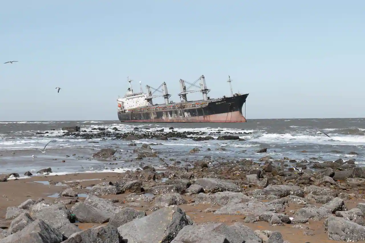 Cargo rouillé échoué au large d'une côte rocheuse, coque abandonnée battue par les vagues.