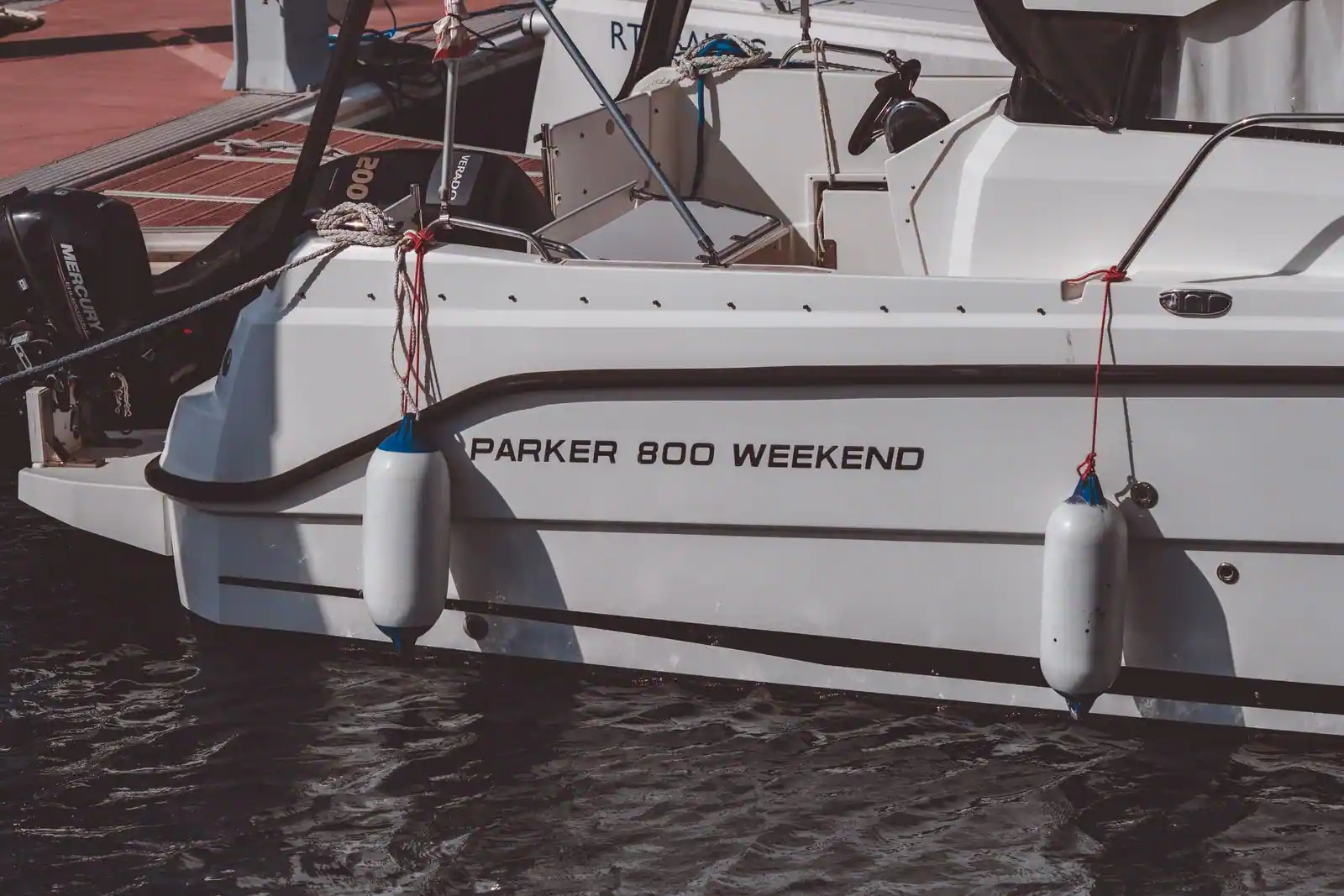 Bateau de plaisance à moteur amarré le long d'un ponton, pare-battages sortis contre la coque blanche.