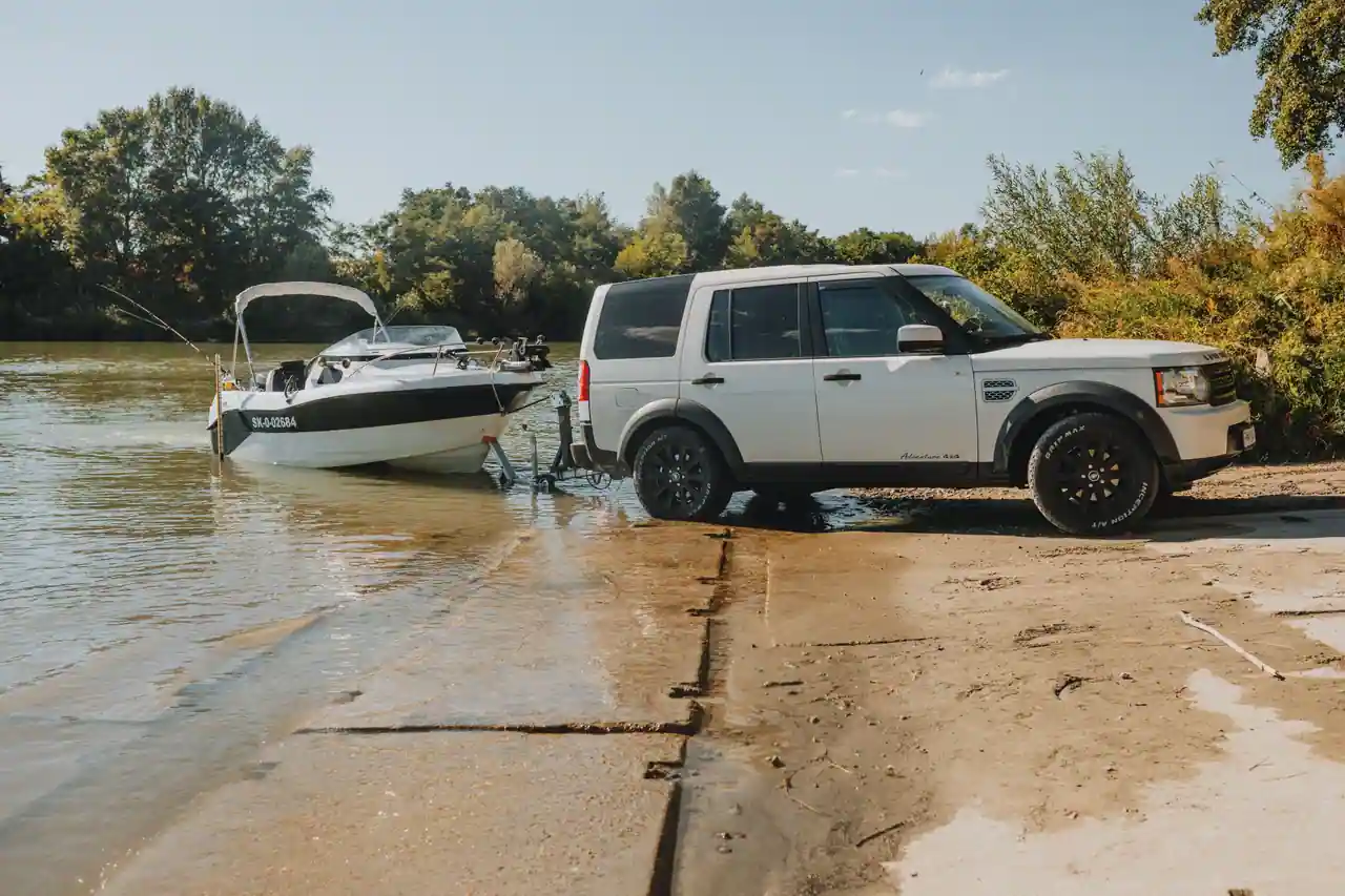 Un 4x4 met un bateau à moteur à l'eau depuis sa remorque, sur une cale au bord d'une rivière.