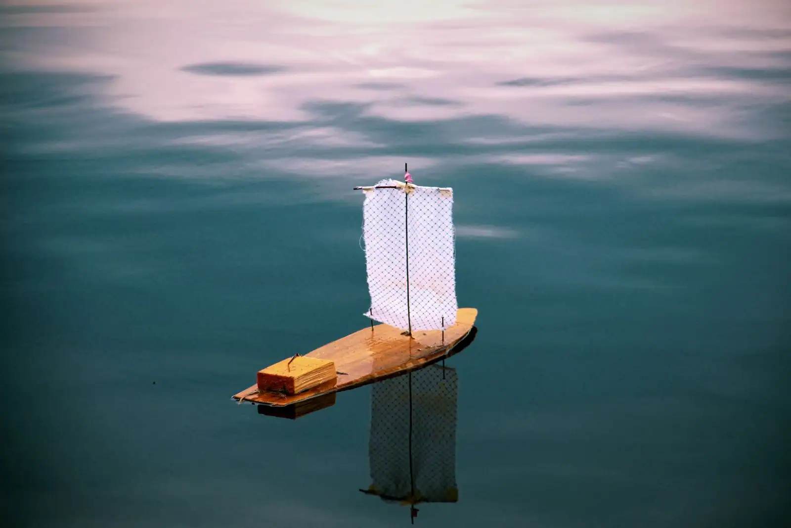 Petit voilier de fabrication artisanale flottant sur une eau calme, son reflet visible sous la coque.