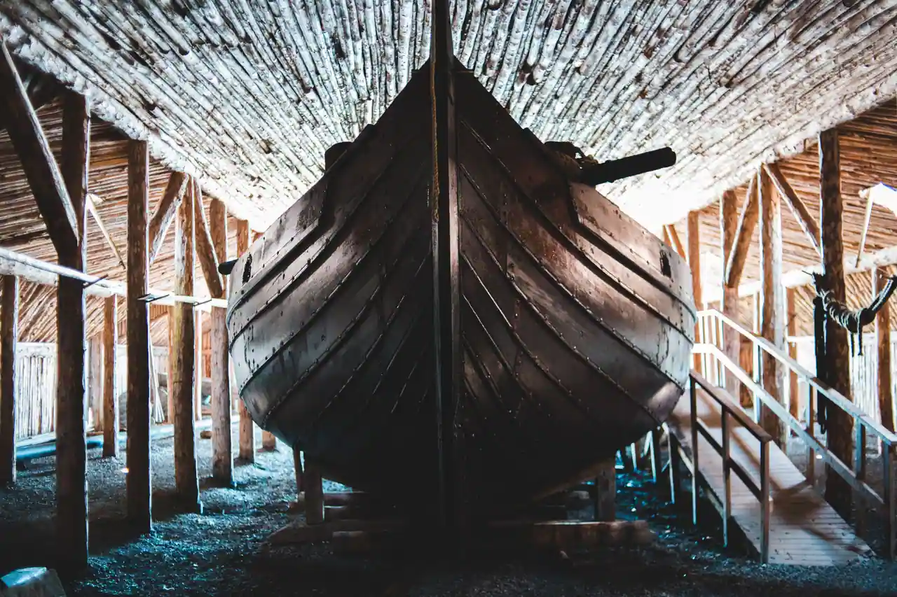 Coque en bois d'un navire viking reconstitué, bordé à clin et rivets visibles sous un abri de charpente.