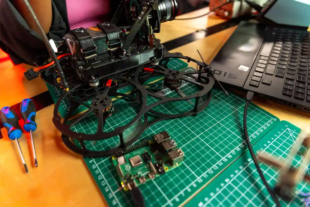 Drone FPV en cours d'assemblage sur un tapis d'atelier, batterie et moteurs de modélisme apparents.