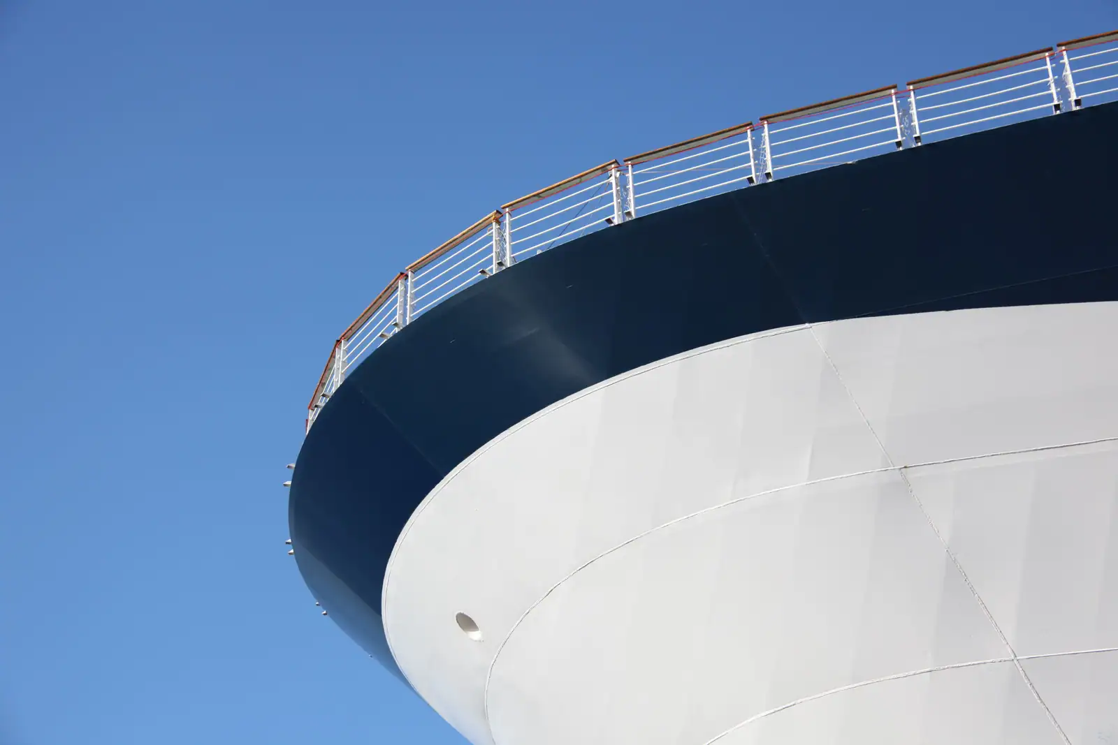 Coque d'un grand navire à passagers vue en contre-plongée, bastingage à main courante bois sur ciel bleu