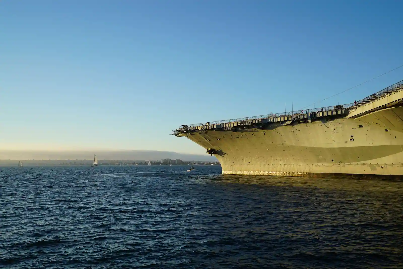 La proue et le débord du pont d'envol d'un porte-avions à quai, vus depuis le plan d'eau.