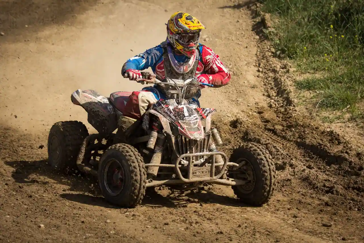 Quad sport monoplace en pleine accélération sur une piste de terre, pilote en tenue et casque intégral.
