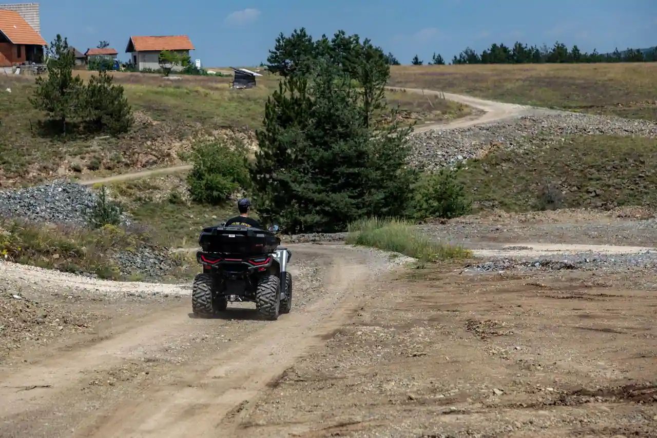 Quad noir de randonnée remontant une piste de gravier sinueuse sur un plateau rural