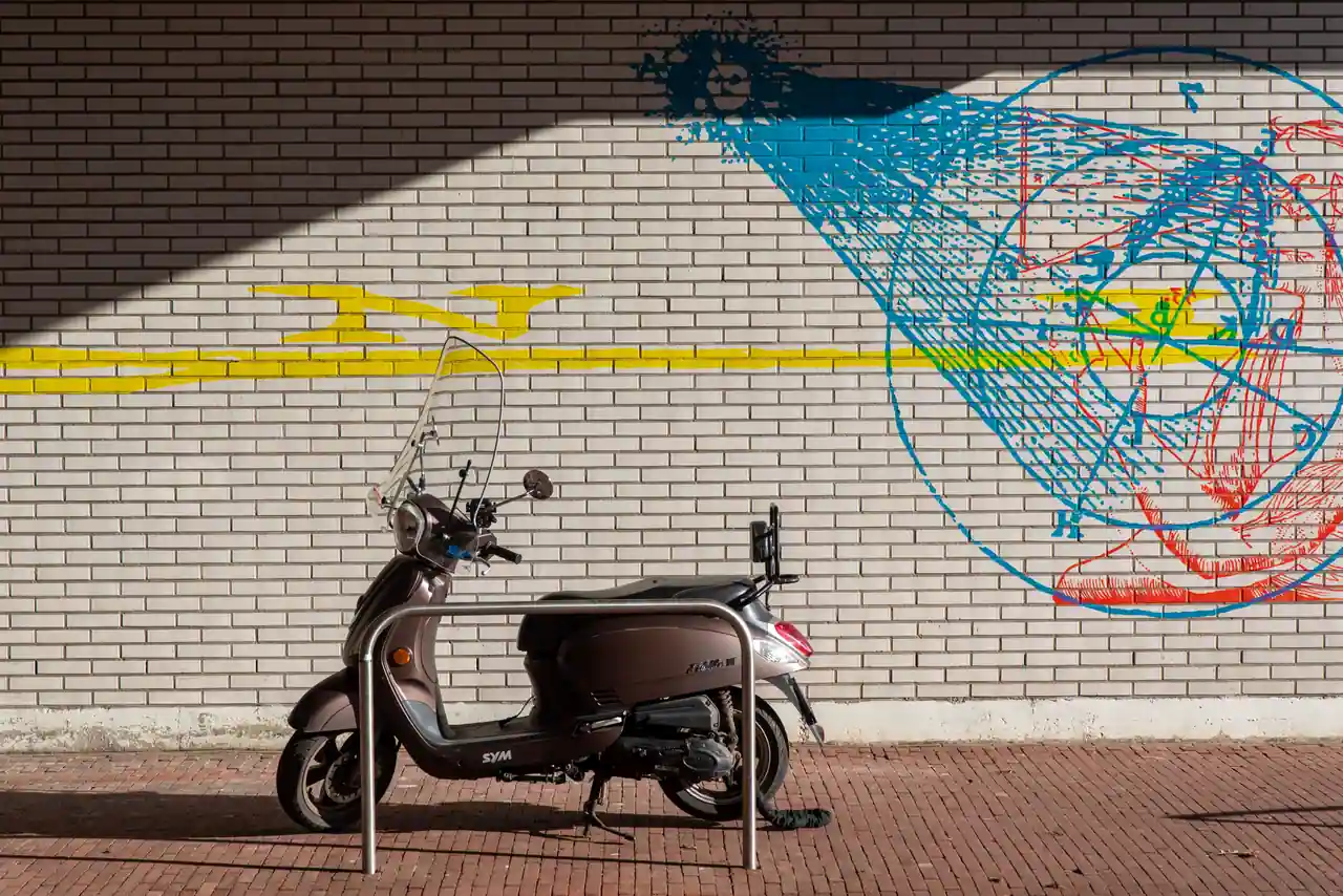 Scooter de ville de style classique stationné de profil le long d'un mur de briques, sur un trottoir pavé
