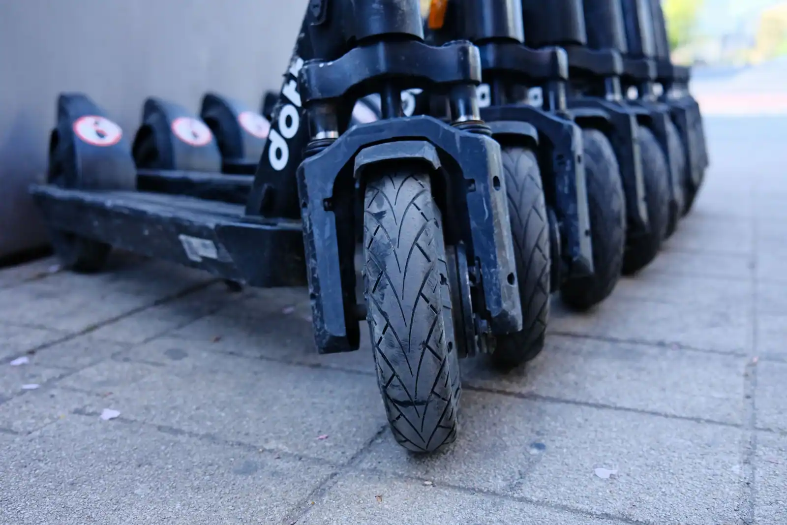 Roues avant et plateaux de trottinettes électriques alignées sur un trottoir, vues au ras du sol