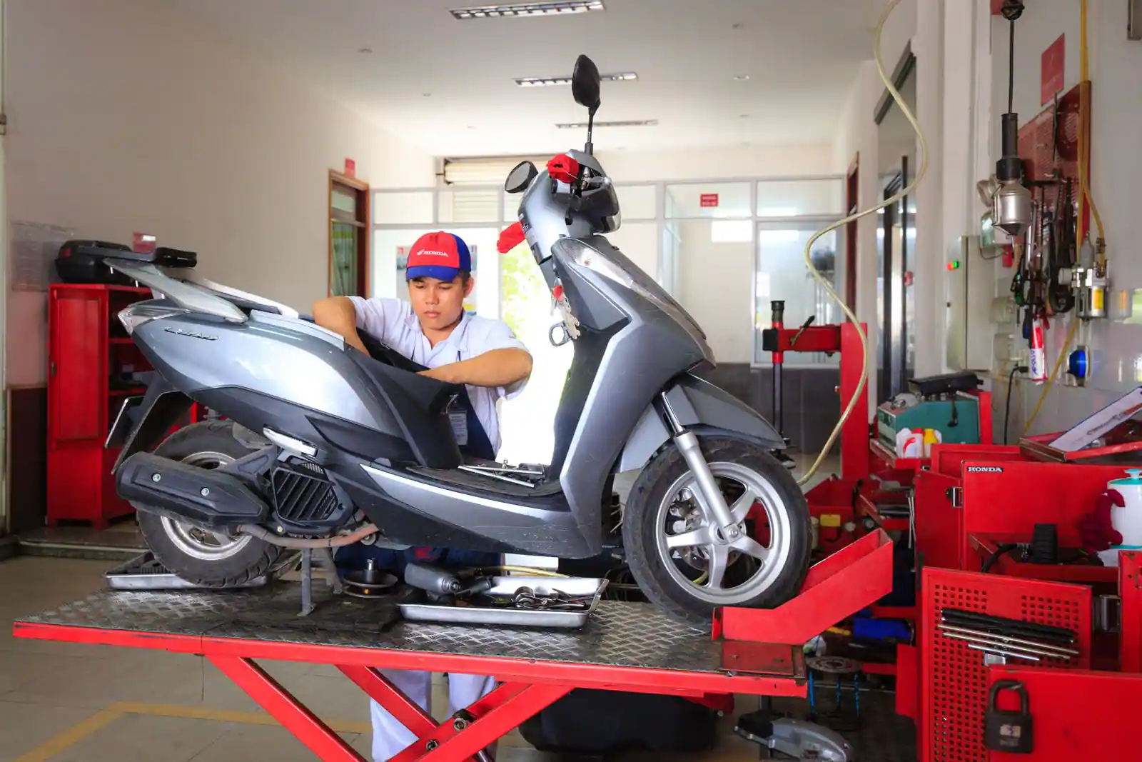 Un technicien intervient sur un scooter Honda posé sur le pont élévateur d’un atelier de la marque.