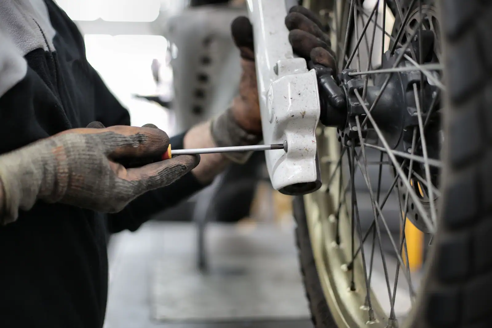 Mains gantées d'un mécanicien intervenant au tournevis sur la roue d'un deux-roues, dans un atelier