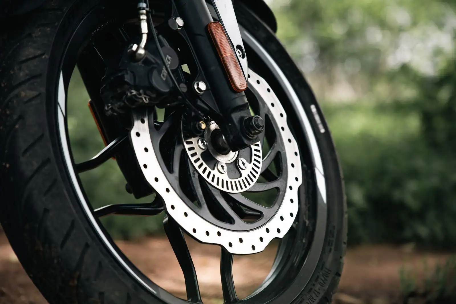 Roue avant d'un deux-roues motorisé, disque de frein perforé et inscriptions de dimension sur le flanc du pneu.